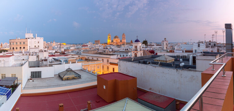 White buildings and historic church towers extend across the center of Cadiz, Spain, with the cathedral illuminated after sunset.
