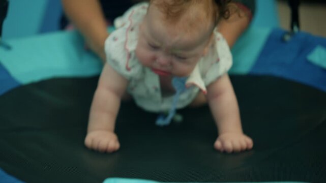 Baby girl with Down syndrome crawling on a small trampoline during physical therapy, focusing on motor skill development