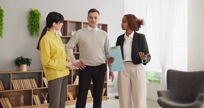Agent meets couple buyers for apartment viewing. Realtor guides a consultation and property tour as clients review features, budget and options. Concept focuses on real estate guidance.
