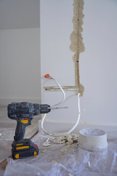 Cordless drill stands beside exposed electrical cables and channels cut into wall