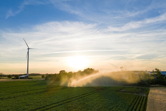Crop cultivation. Wind turbines farm. Green energy. Sprinkler irrigation system watering field. Wind mill for renewable electric energy production. Irrigation system and windmill in rural area