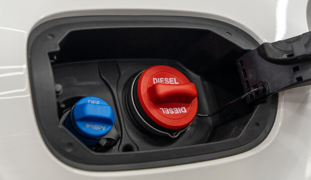 Close-up of open car fuel filler neck with red diesel cap and blue AdBlue DEF fluid cap inside white vehicle. Detailed view of modern diesel automobile refueling tank system. Concept of automotive. 