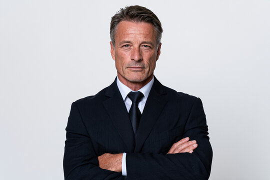 Professional studio headshot of a confident middle aged businessman in a formal dark suit and tie, arms crossed, looking at the camera, isolated on a light gray background for corporate portrait use.