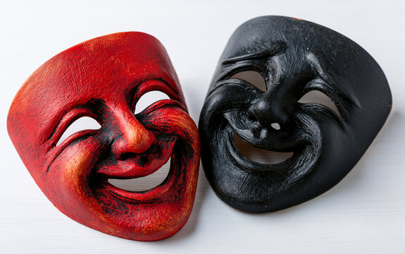 Two theatrical masks, one red and one black, with smiling faces symbolize joy and sorrow. Dramatic art faces express emotions, duality of human nature.