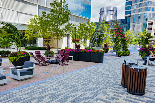 Wide paved public plaza connects modern shops, residences, seating, and flower displays.