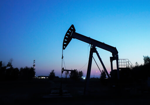 Pumpjack in oil well of oil field in night. Industrial crude area. Crude pump jack working on oil field on sunset. Pumpjack, Oil drill rig, drilling derrick in oilfield. Crude petroleum industry.