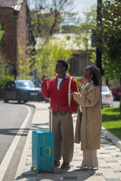 Curious tourists black male and female married couple walk along city downtown searching path to hotel, young couple african american man and woman travelers standing on street looking around new town