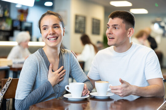 Young guy and a woman are sitting at a table in a cafe and talking, they make joint plans for traveling around Europe. Woman and man on a date drinking coffee