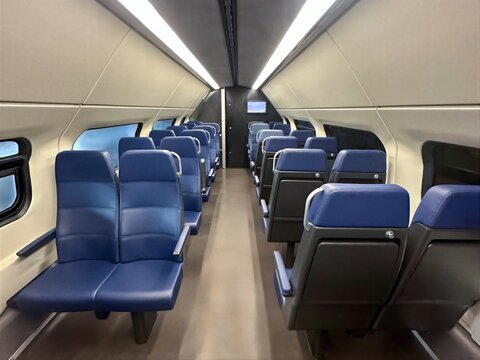 Empty interior of a modern passenger train cabin with rows of comfortable blue seats and bright overhead lighting
