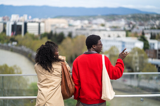 African american man and woman tourists visiting attractions in new city, married couple enjoying landmark view from high viewpoint, male and female partners travelers observing urban city from hill.
