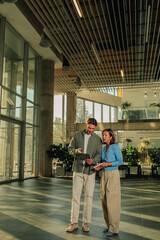 Obraz na płótnie Canvas Diverse business partners collaborating, discussing project on tablet in modern office atrium, teamwork and innovation