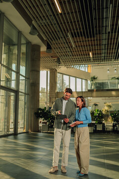 Diverse business partners collaborating, discussing project on tablet in modern office atrium, teamwork and innovation