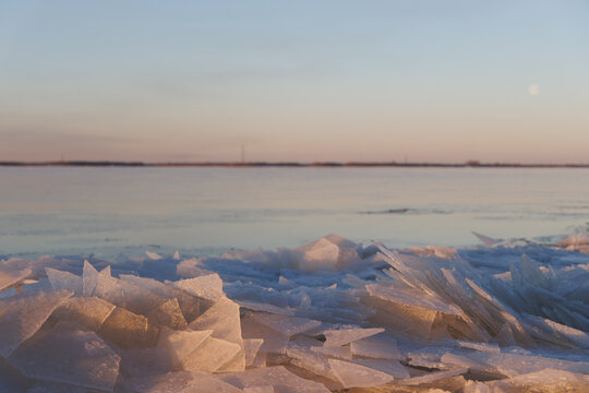 Close up scenery of broken ice shards and crystals on a northern coast covered with pastel golden and pink twilight sun light.