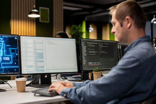Engineer in a tech startup office automates repetitive tasks with AI scripts on a PC while using an artificial intelligence program to speed up feature implementation and software work.
