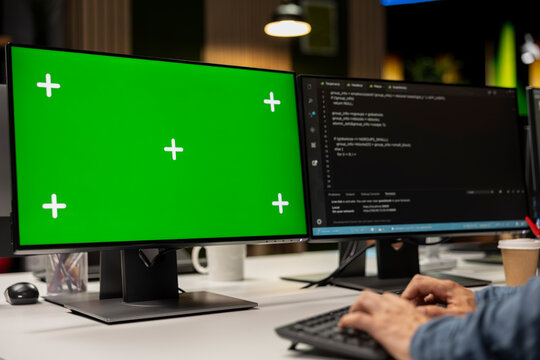 Technician uses a green screen PC to write code and debug software issues while improving system stability in a tech startup office with a mockup display.