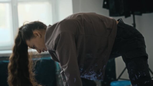 Young adult Caucasian female artist using crumpled fabric to texture purple paint on large canvas on floor, handheld tilt up. Clip is perfect for creative industry promos and art school ads