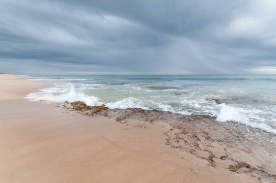 Dark storm clouds gather above a deserted shoreline as distant rain falls over the sea