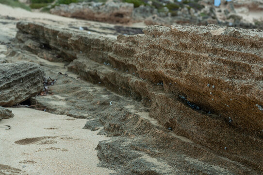 Layered coastal rocks shaped by erosion on a sandy beach
