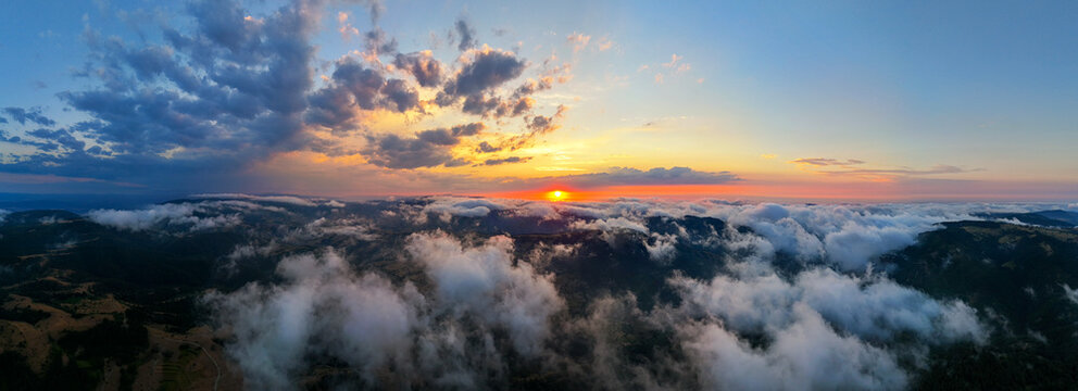 Panoramic aerial view above sea of clouds and green mountains during golden hour sunset in Sinop, Turkey. Stunning natural landscape with glowing sunbeams breaking through dramatic sky and cloudscape.