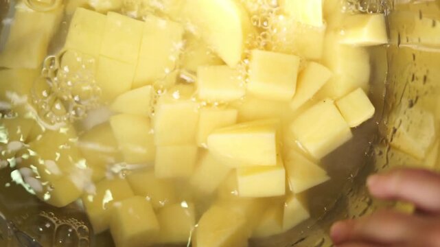 Upside view of diced potatoes being washed under running water in a steel bowl. 
