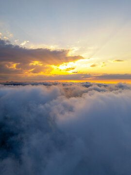 Aerial vertical view above fluffy clouds during golden hour sunset in Sinop, Turkey. Stunning natural landscape with glowing sunbeams breaking through dramatic sky and serene cloudscape panorama.