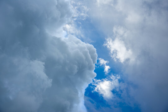 Majestic storm clouds forming and gathering in the blue sky. Dramatic cumulus and cumulonimbus cloud formations changing shape before a heavy summer rainfall or thunderstorm.