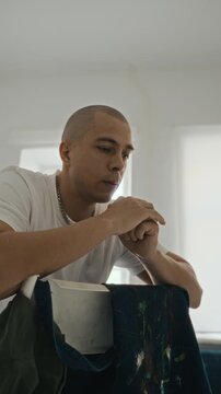 Vertical video of young adult Caucasian man leaning on chair and planning next painting in art studio. Footage is suitable for creative agency marketing or art school promotions