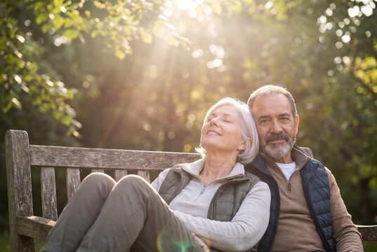 Senior couple (a man and a woman) resting on a wooden park bench during a sunny afternoon