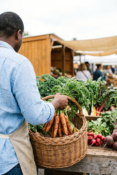 Man placing fresh leafy carrots into a wicker basket at farmers market