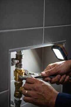 The hands of a technician working on a main water riser pipe assembly near a bathroom wall nook