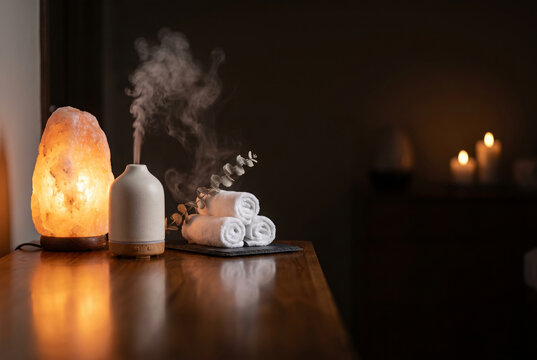Glowing natural salt lamp placed on a dark teak wood counter next to an ceramic essential oil
