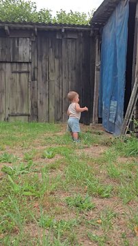 Little baby boy taking his first steps walking alone on grass outdoors in rural countryside landscape during summer day rear view back concept.