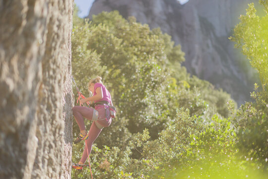 Woman rock climbing a mountain in sunny conditions