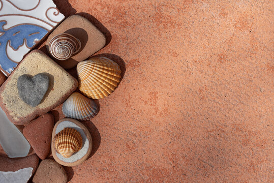 Shells and ceramic shards lie at the edge of a large terracotta tile. The shards are positioned along the side of the tile. It is a background with plenty of space for text.