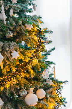 Snow covered Christmas tree decorated with white ornaments, star decorations, clear baubles and warm glowing garland lights in a bright winter interior. Holiday mood, festive aesthetic atmosphere