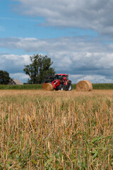 Red tractor working in a harvested agricultural field, farm machinery for farming and crop production under dramatic cloudy sky © Iryna