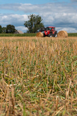 Red tractor working in a harvested agricultural field, farm machinery for farming and crop production under dramatic cloudy sky © Iryna