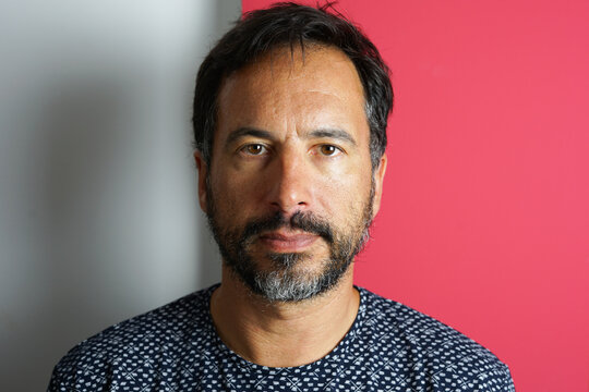 Face of a 37-year-old Moroccan man against a white and red wall background.