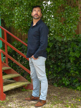 White man, dark-skinned, thin, 40 years old, casually dressed, posing against a backdrop of colorful wooden houses.