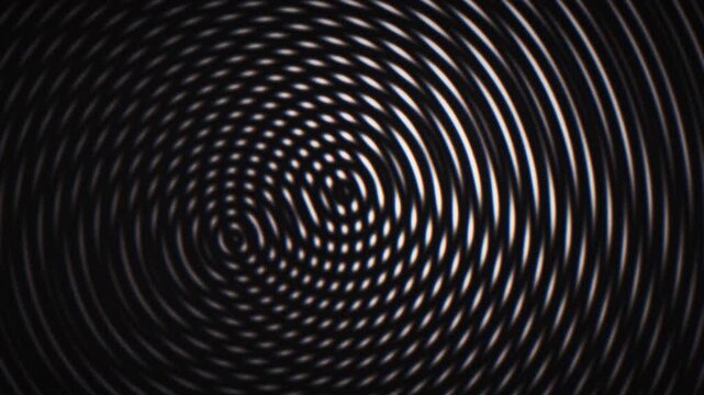 Grainy loop animation of concentric ripple rings forming an abstract moire pattern on a dark background. Ideal for tech, music, and futuristic motion graphics.