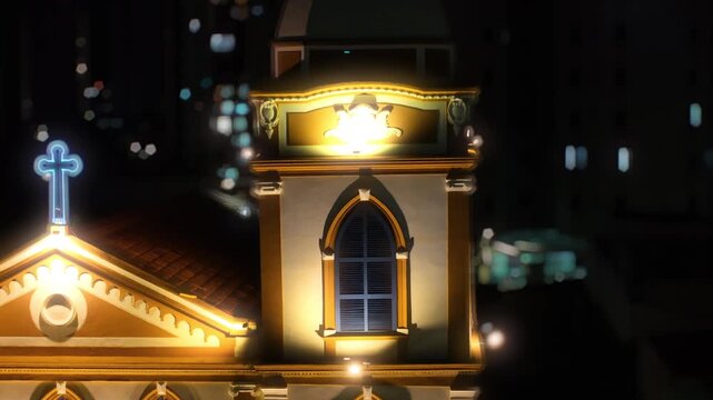 4K night video of S&atilde;o Benedito Church illuminated among urban buildings in downtown Mogi das Cruzes, S&atilde;o Paulo, Brazil, with city traffic.

