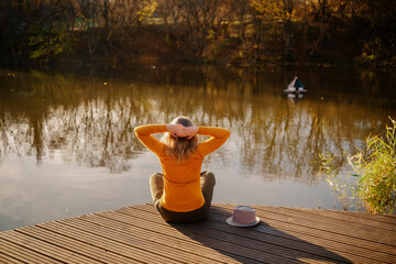 Fototapeta premium Woman traveler from back on wooden dock at autumn lake Concept of relaxation peaceful outdoor recreation mental health recovery