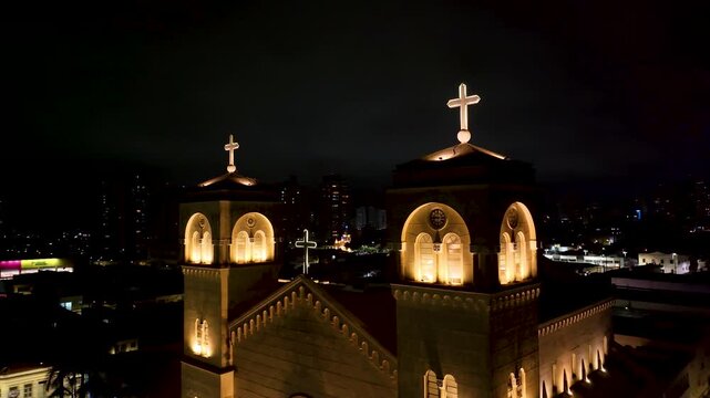 4K aerial night view of an illuminated historic Catholic church in downtown Mogi das Cruzes, S&atilde;o Paulo, Brazil, surrounded by city lights.