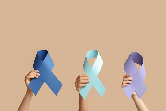Cancer awareness and support hands holding blue light blue and purple ribbons for various causes on a beige background