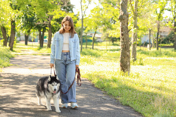 Pet ownership and healthy lifestyle, young woman walking a siberian husky dog on a leash in a sunny park © Pixel-Shot