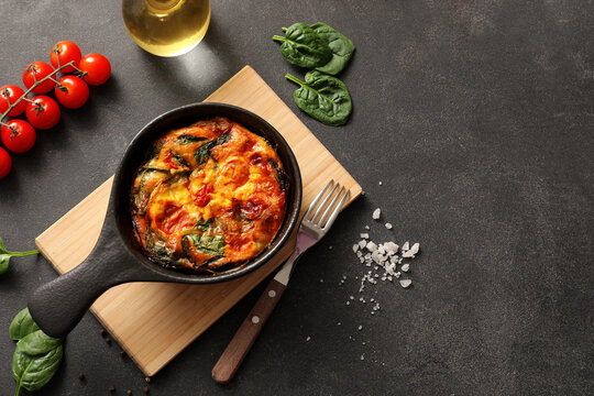 Frying pan with delicious frittata and ingredients on dark grey table