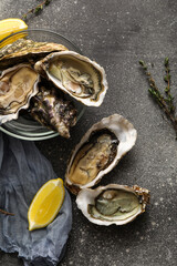 Glass bowl with delicious fresh oysters, lemon and thyme on dark background © Pixel-Shot