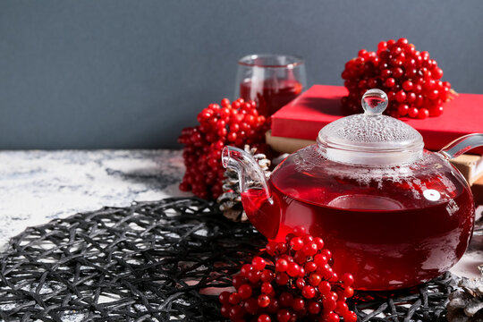 Glass teapot of hot viburnum tea with cones on grunge table against grey wall