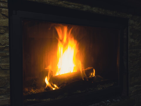 Burning fireplace with glowing flames behind glass and stone wall
