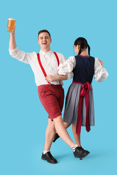 Young happy couple in traditional German clothes with mug of beer dancing on blue background